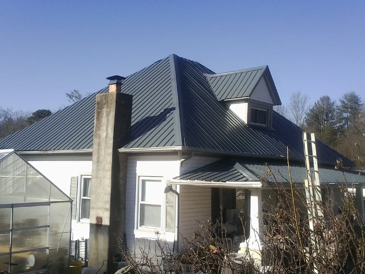 Dark blue standing seam metal roof on a white farmhouse with dormer — Slate & Tile Roof Repair by Roofing Brothers in Callahan