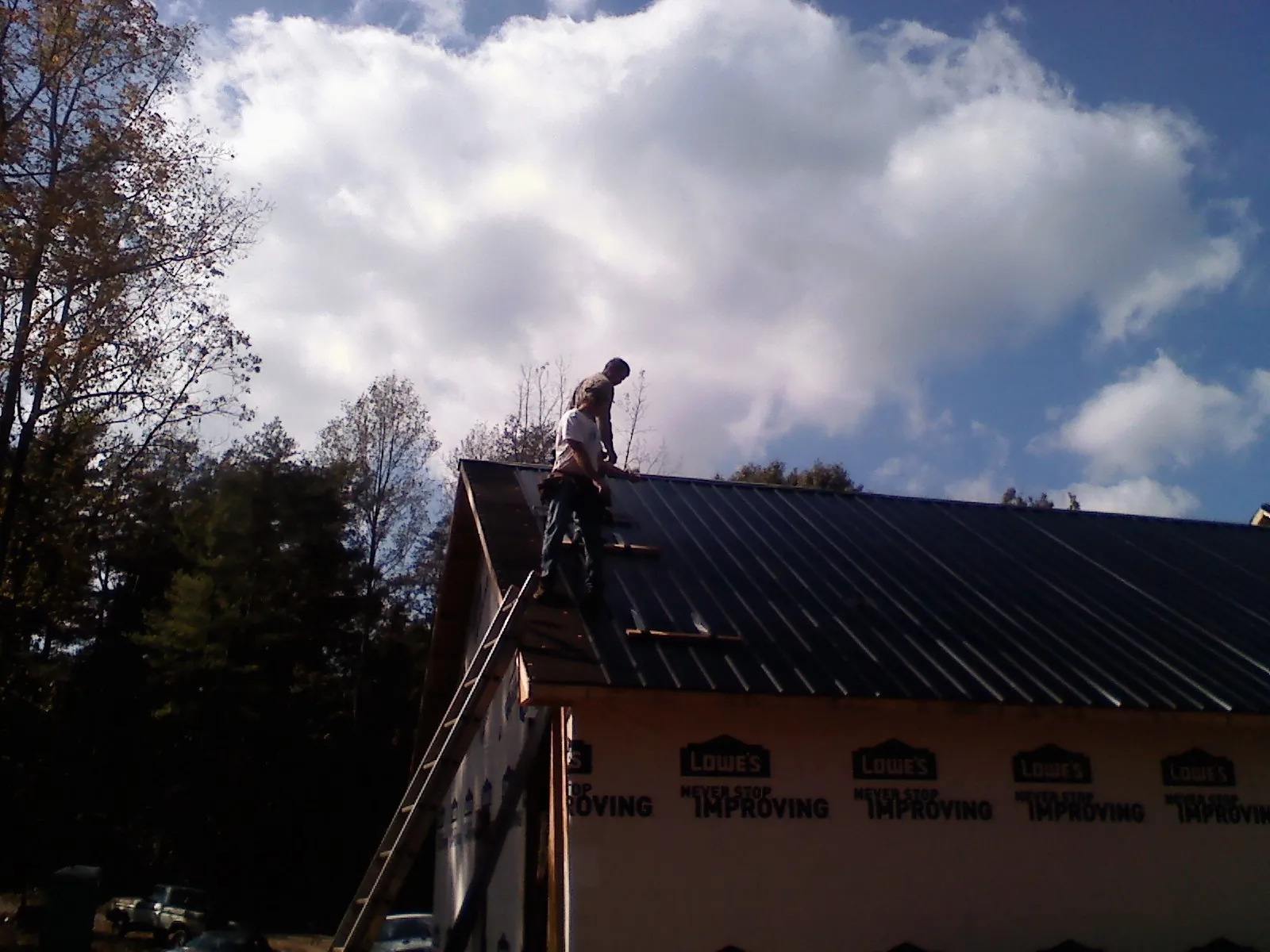 Roofer fastening dark metal panels high against a cloudy sky, from a Roof Inspection job in Callahan